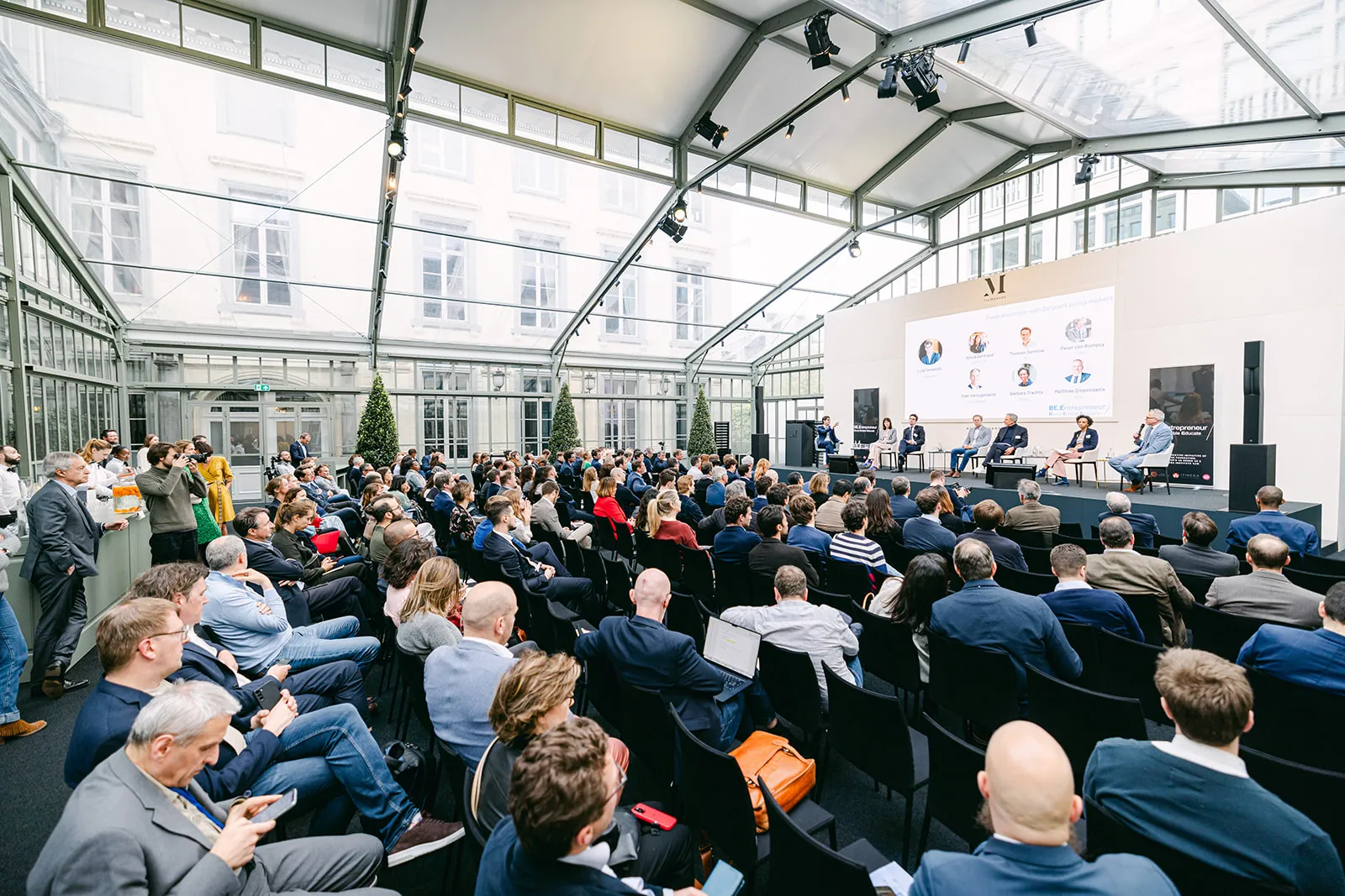 La séance plénière BE.Entrepreneur d'avril 2024 : une salle comble sous une verrière à TheMerode, à Bruxelles, avec un panel sur scène.