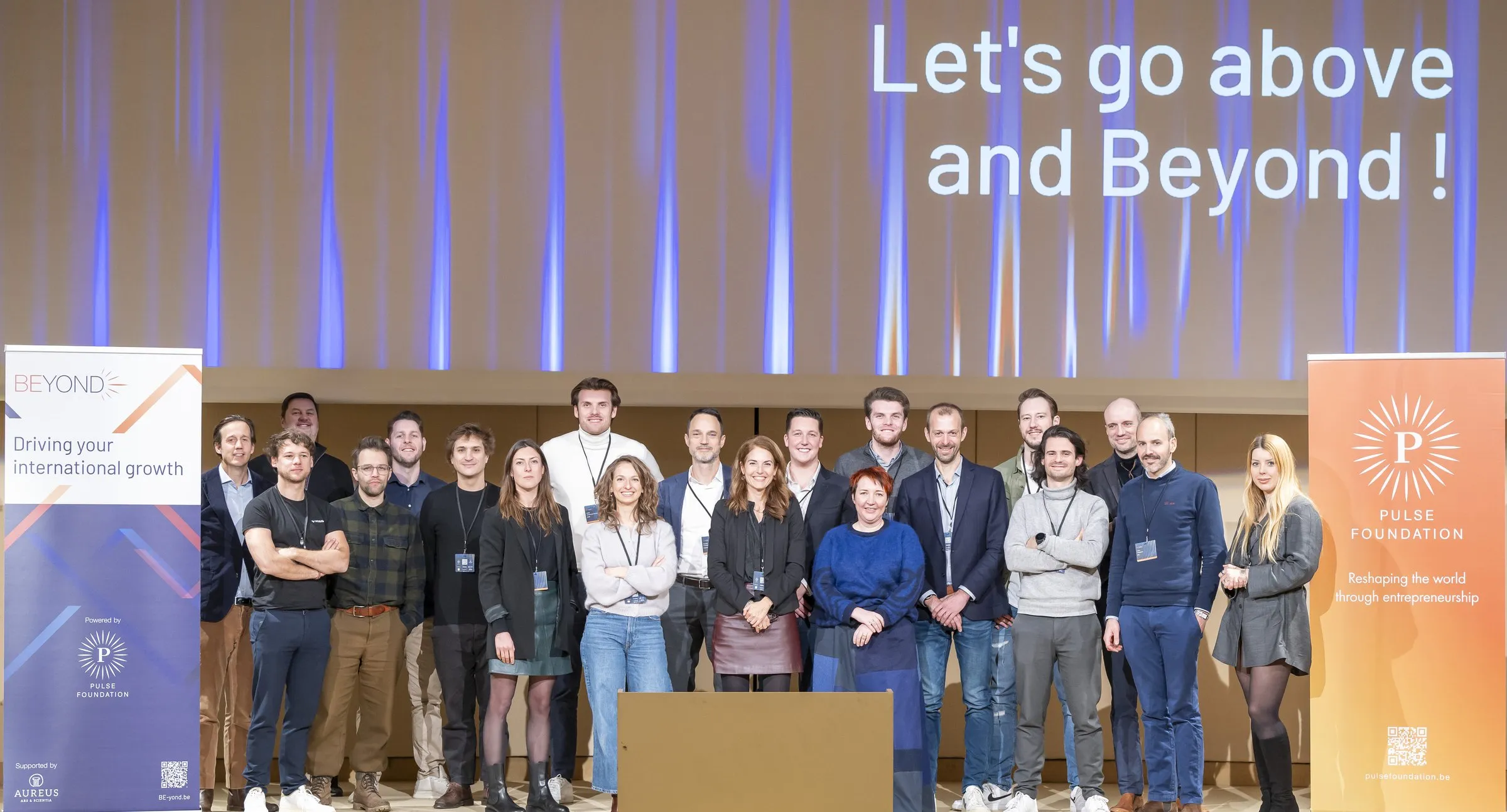 The BEyond cohort on stage at the kick-off, under a screen reading Let's go above and Beyond