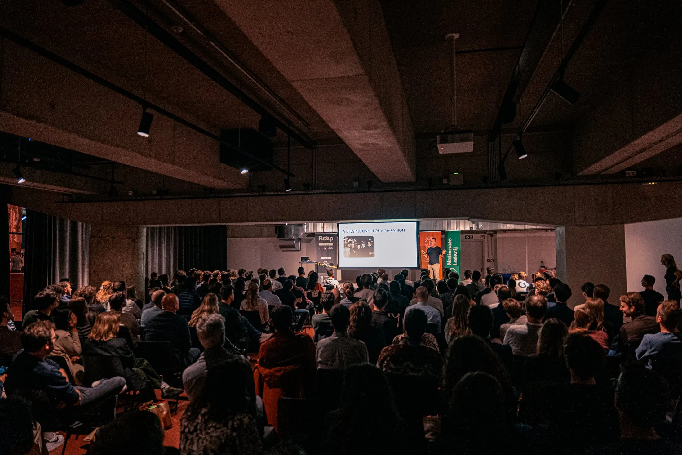 A full room at a Fuckup Nights evening in Belgium, watching a founder talk through what went wrong.