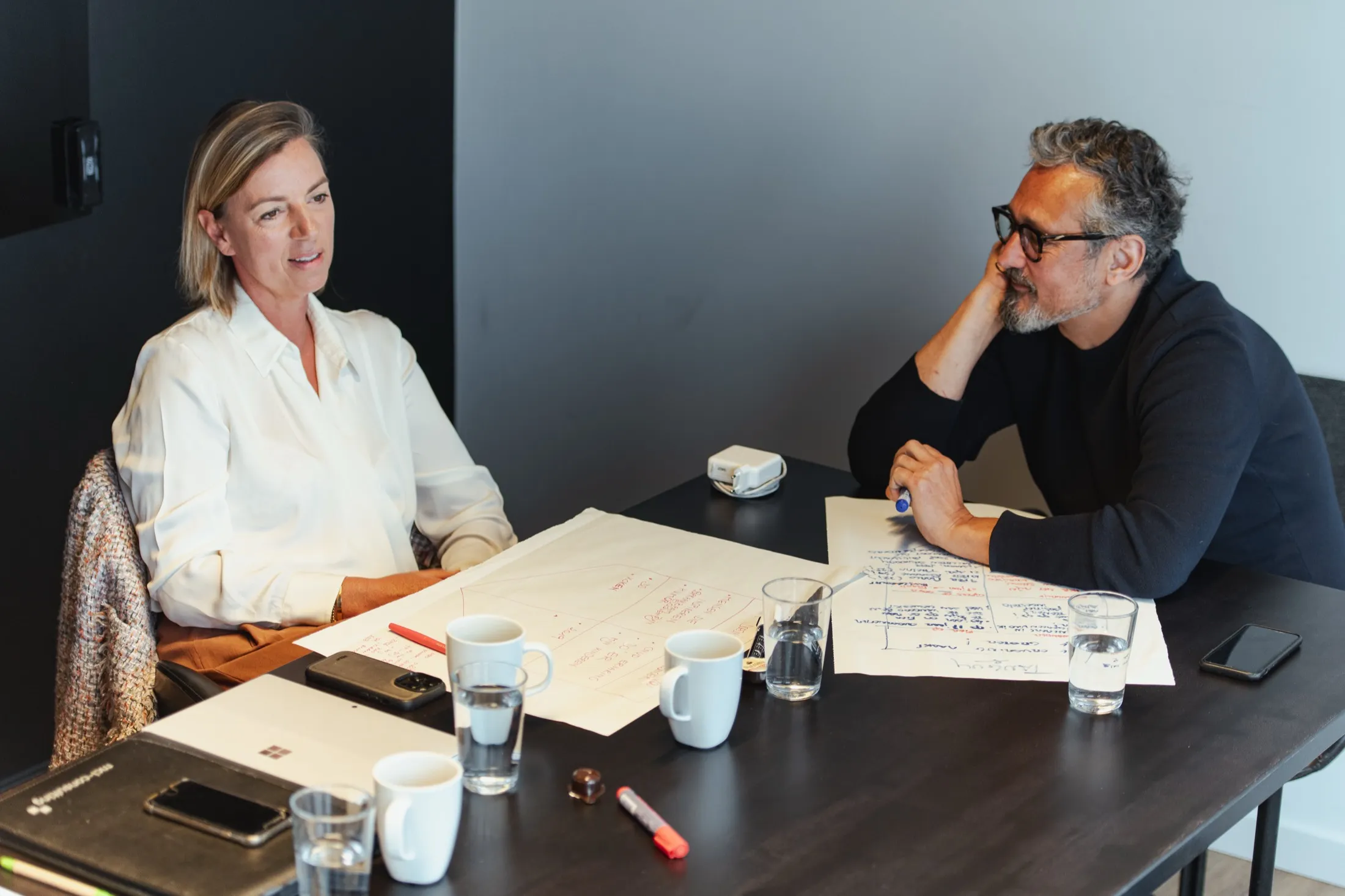 Deux personnes discutent de part et d’autre d’une table couverte de notes