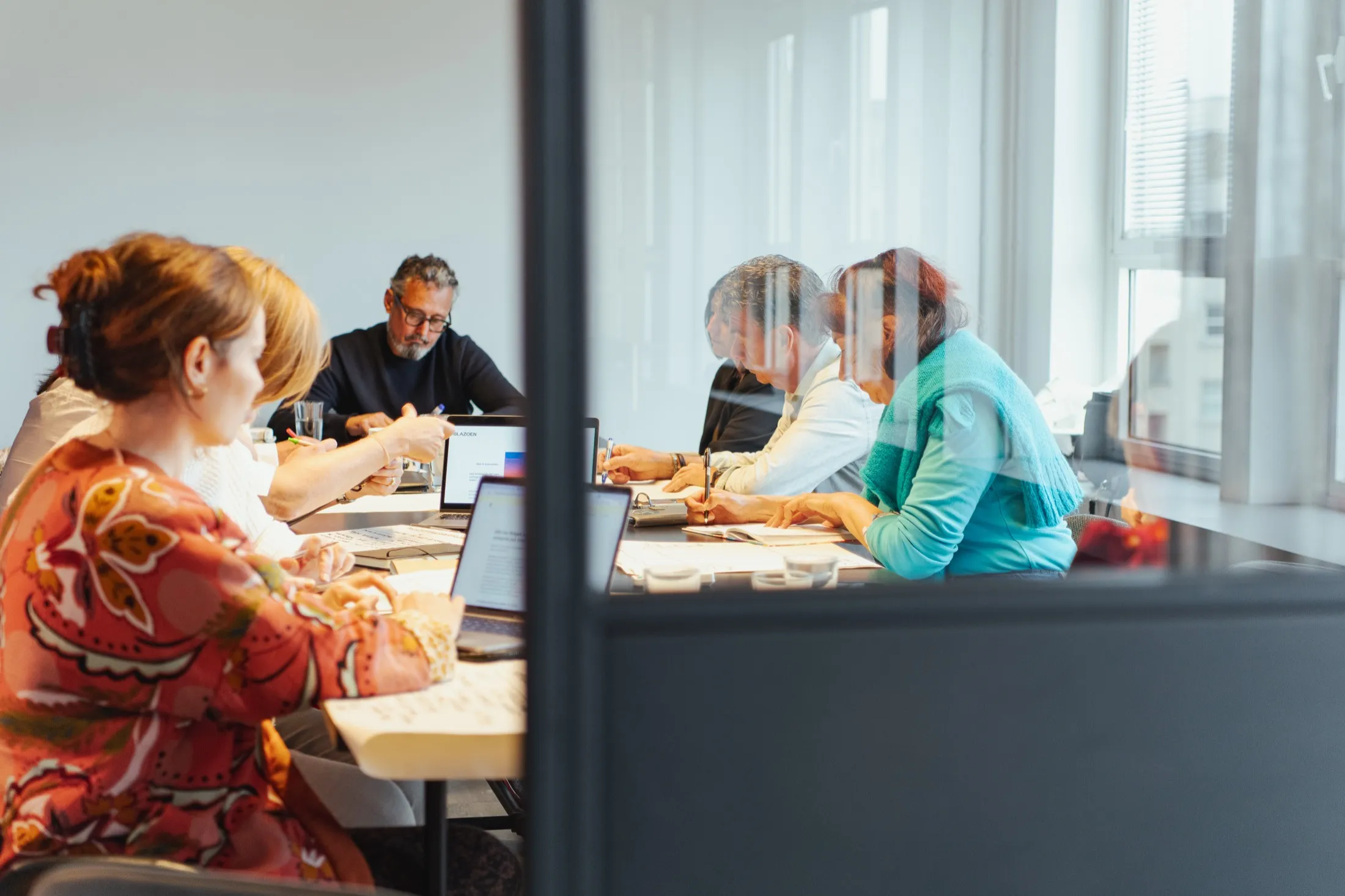 The group at a table in daylight, seen through a glass wall